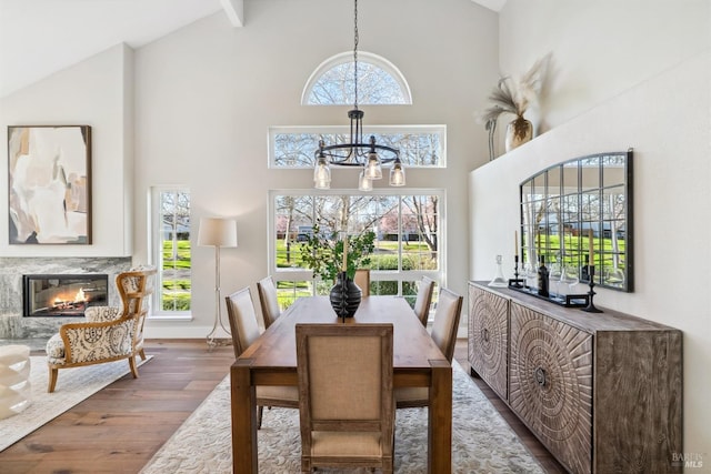 dining area featuring wood finished floors, a premium fireplace, beam ceiling, high vaulted ceiling, and a notable chandelier