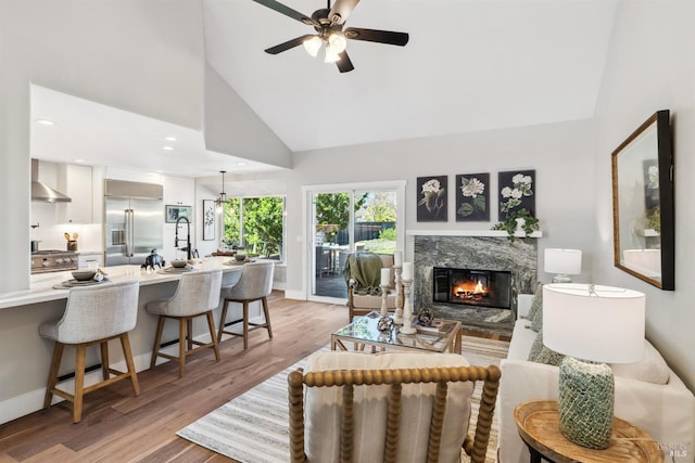 living area with light wood-style floors, a high end fireplace, ceiling fan, high vaulted ceiling, and baseboards