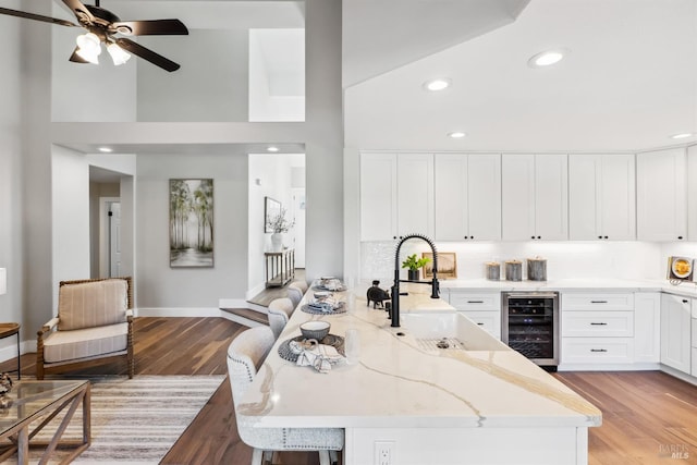 kitchen featuring wine cooler, a peninsula, light stone countertops, light wood-style floors, and white cabinetry