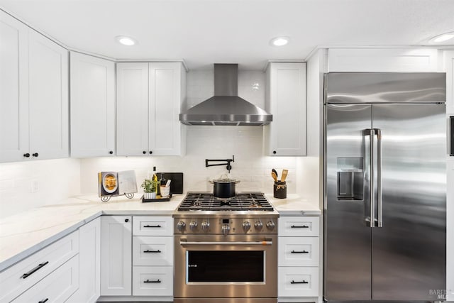 kitchen featuring backsplash, high end appliances, wall chimney exhaust hood, and white cabinets