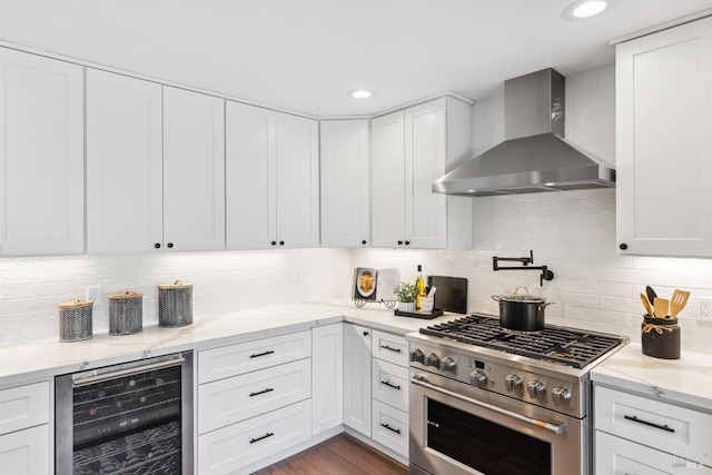 kitchen with beverage cooler, white cabinets, high end stainless steel range oven, and wall chimney range hood