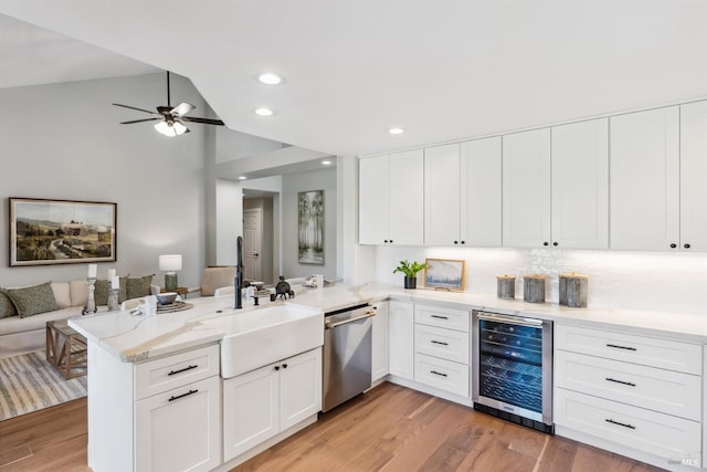kitchen with stainless steel dishwasher, a sink, open floor plan, a peninsula, and wine cooler