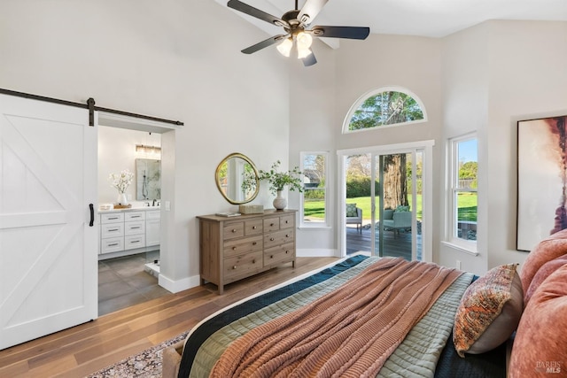 bedroom with a barn door, a towering ceiling, ensuite bath, wood finished floors, and access to outside