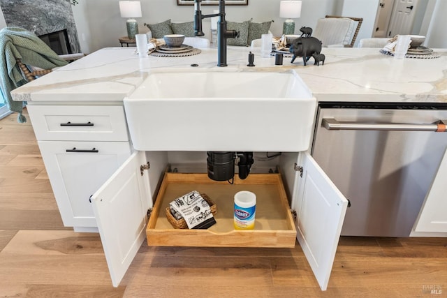 details featuring white cabinets, stainless steel dishwasher, a sink, light stone countertops, and light wood-style flooring