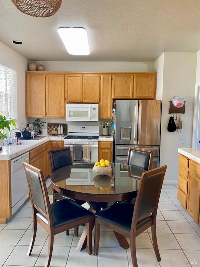 kitchen with light tile patterned floors, tile counters, a sink, a textured ceiling, and white appliances