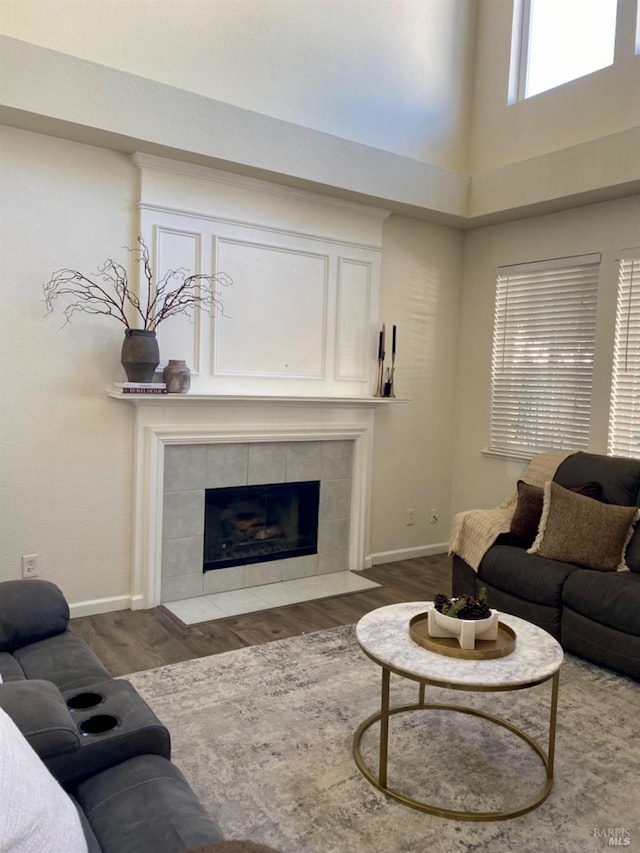 living area featuring a tiled fireplace, wood finished floors, and baseboards