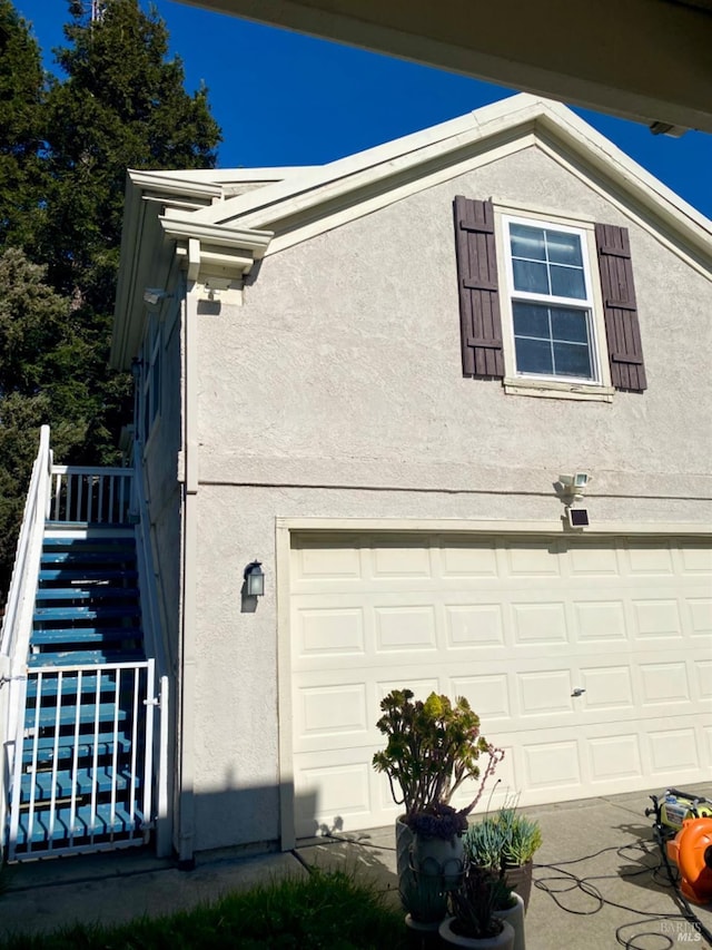 view of side of property with stairway, an attached garage, and stucco siding