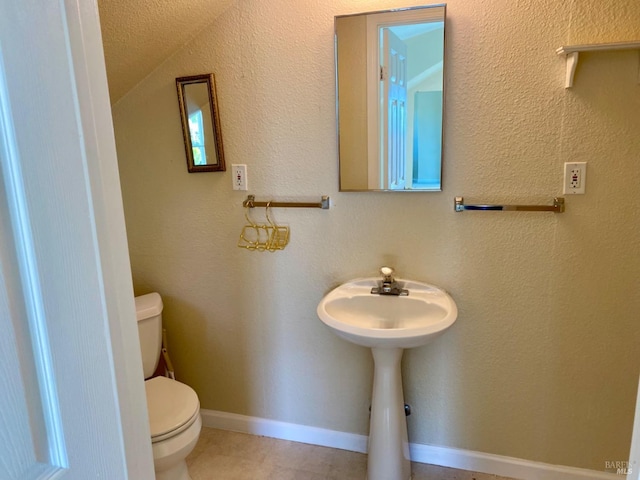 half bath featuring baseboards, a textured wall, and toilet