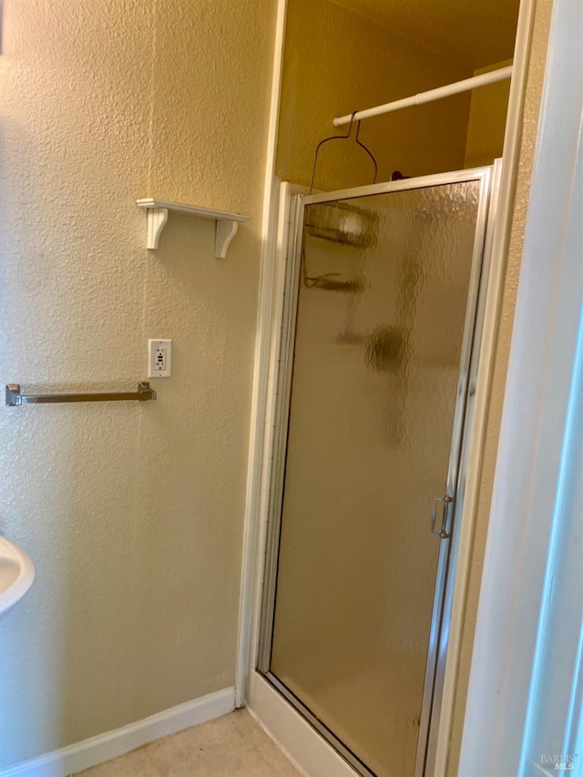 bathroom with a stall shower, a textured wall, baseboards, and tile patterned floors