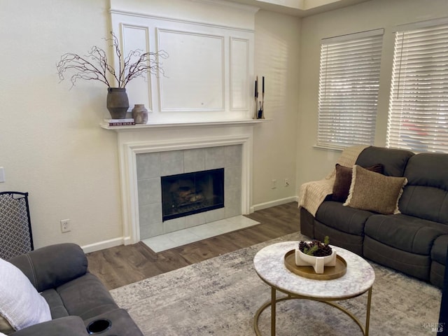 living area with a tile fireplace, wood finished floors, and baseboards