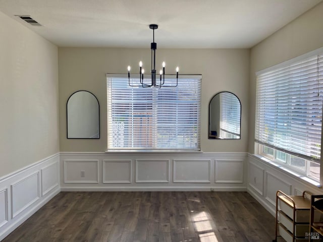 unfurnished dining area with a wainscoted wall, a notable chandelier, visible vents, and dark wood-style flooring