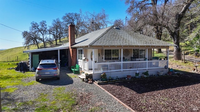 view of front of home with a shingled roof, a chimney, gravel driveway, covered porch, and a carport