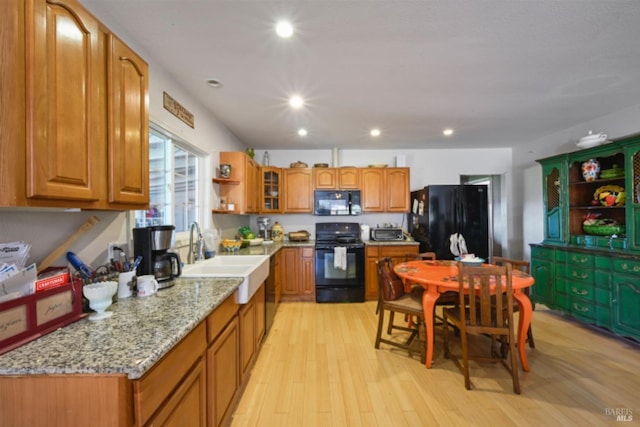 kitchen featuring light wood-style flooring, brown cabinets, light stone countertops, black appliances, and a sink