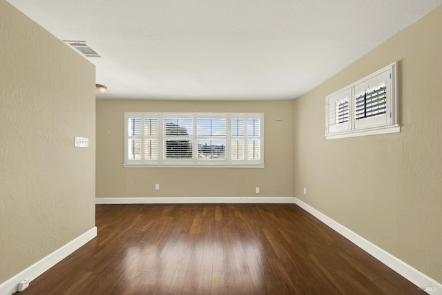 spare room featuring a wealth of natural light, wood finished floors, visible vents, and baseboards