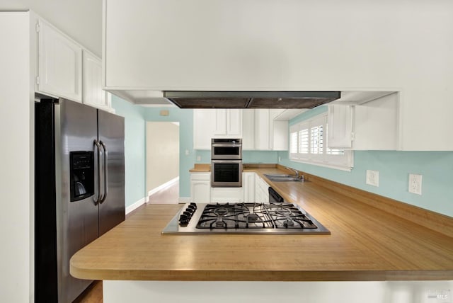 kitchen with white cabinets, appliances with stainless steel finishes, a peninsula, light countertops, and a sink