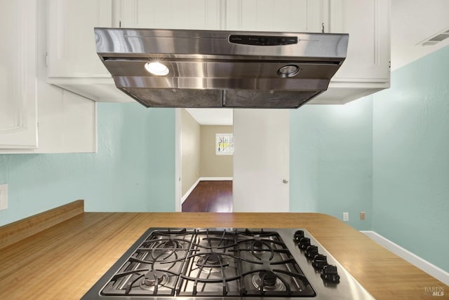 kitchen featuring baseboards, white cabinets, visible vents, and wall chimney exhaust hood