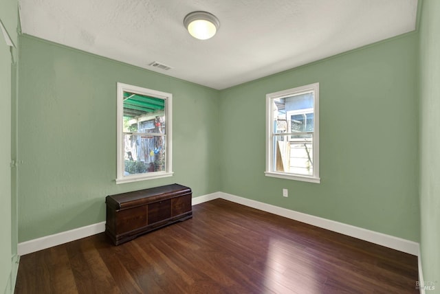 spare room featuring dark wood-type flooring, visible vents, and baseboards