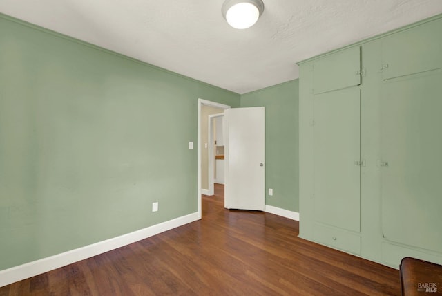 unfurnished bedroom featuring baseboards, dark wood finished floors, and a closet