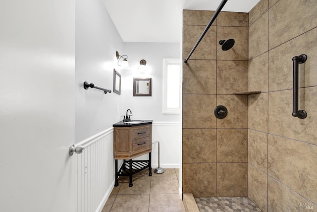 full bathroom featuring tile patterned flooring, vanity, tiled shower, and wainscoting