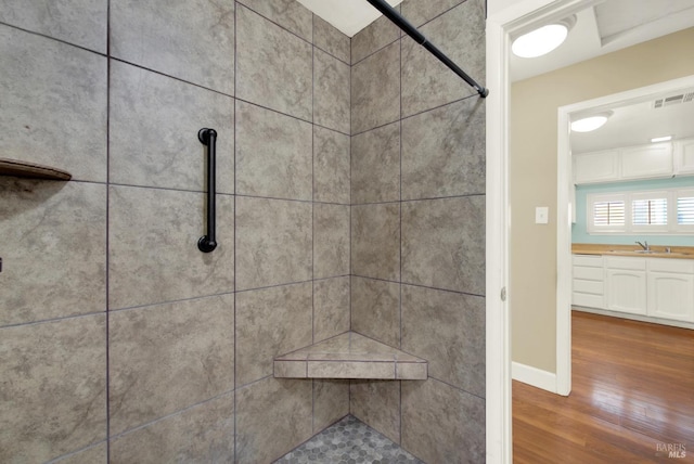 interior details featuring wood finished floors, vanity, visible vents, baseboards, and tiled shower