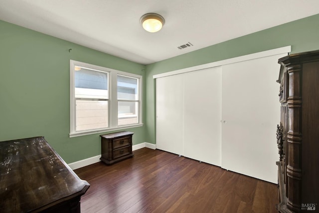 unfurnished bedroom featuring visible vents, a closet, baseboards, and dark wood-type flooring