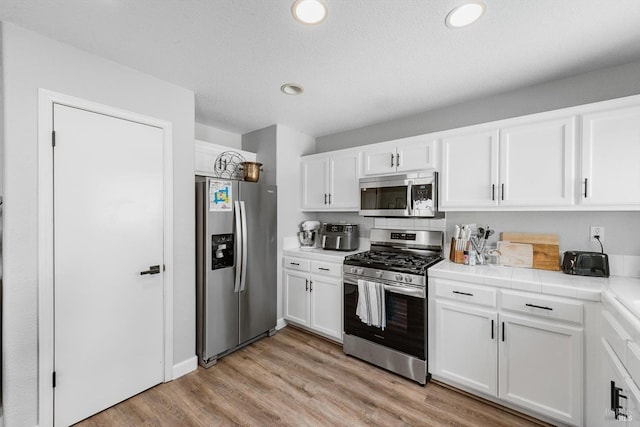 kitchen with recessed lighting, stainless steel appliances, tile counters, white cabinets, and light wood-type flooring