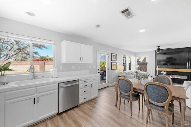 kitchen featuring visible vents, tile counters, dishwasher, white cabinets, and a sink