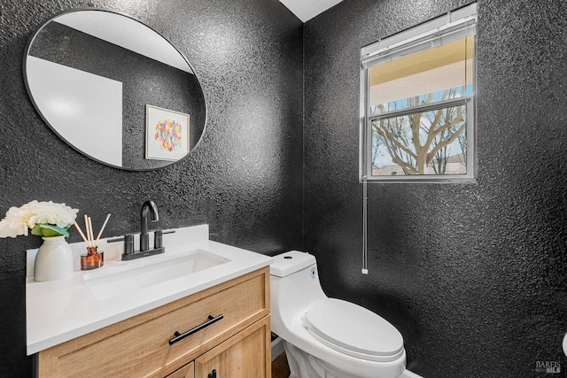 bathroom featuring vanity, toilet, and a textured wall