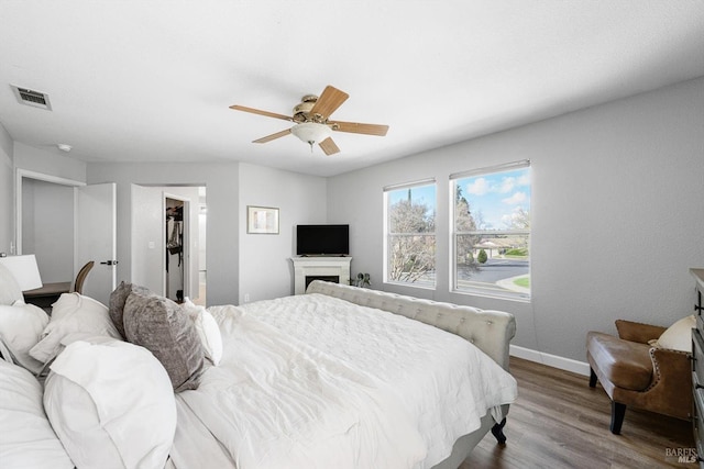 bedroom with visible vents, a walk in closet, a ceiling fan, wood finished floors, and baseboards