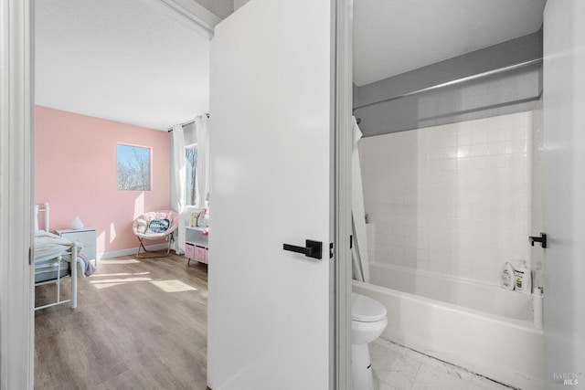 bathroom with baseboards, toilet, wood finished floors, and shower / tub combo