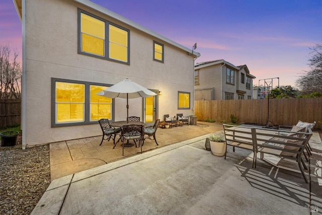 back of property at dusk featuring stucco siding, a patio, outdoor dining area, and fence