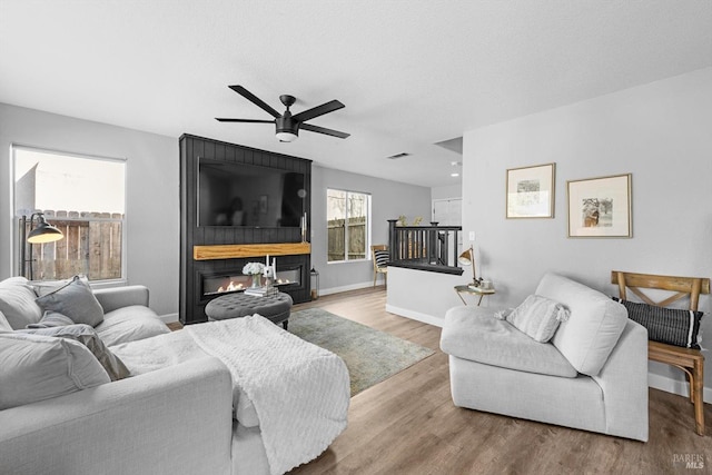 living area with wood finished floors, a ceiling fan, baseboards, visible vents, and a fireplace