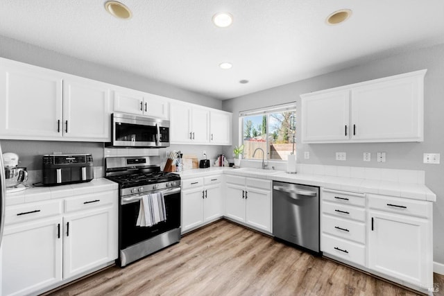 kitchen featuring tile countertops, stainless steel appliances, light wood finished floors, and a sink