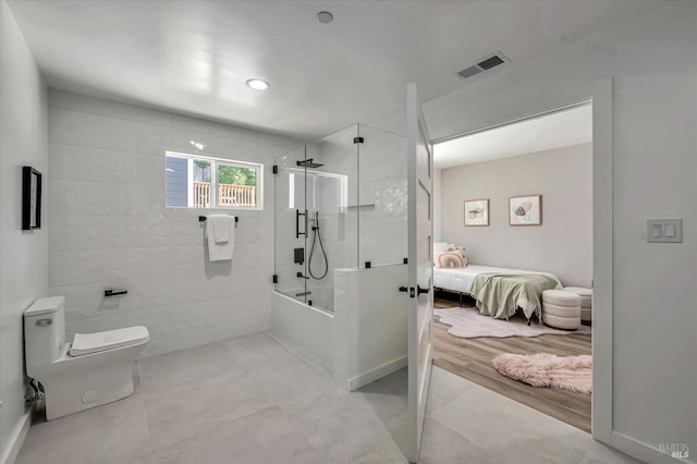 bathroom featuring tile walls, visible vents, toilet, combined bath / shower with glass door, and ensuite bath