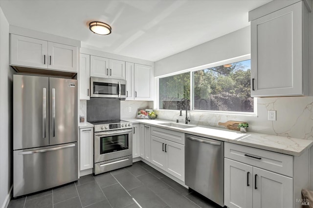 kitchen featuring stainless steel appliances, white cabinets, a sink, and backsplash