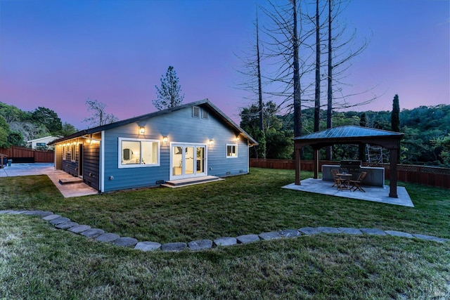 back of property at dusk with a yard, a patio, a gazebo, a fenced backyard, and a jacuzzi