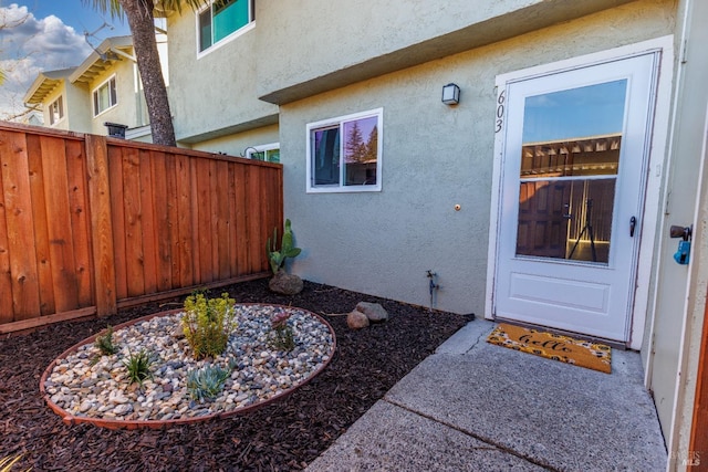 view of exterior entry featuring fence and stucco siding