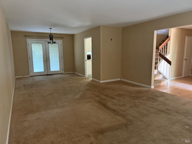 carpeted empty room featuring stairs, french doors, baseboards, and a notable chandelier