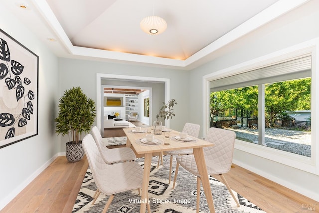 dining space featuring light wood-style floors, a raised ceiling, and baseboards