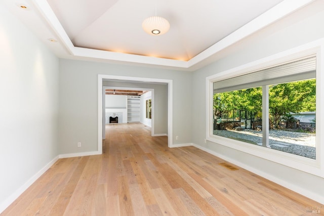 empty room with a tray ceiling, baseboards, a fireplace, and light wood finished floors