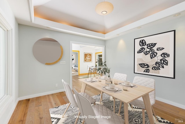 dining room with a tray ceiling, light wood-style flooring, and baseboards