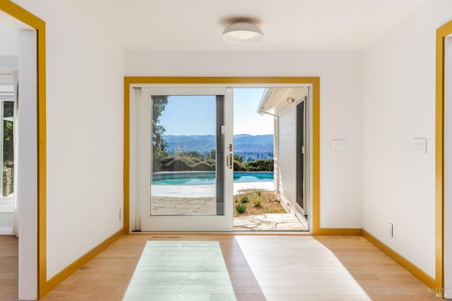 doorway with baseboards, a mountain view, and light wood finished floors