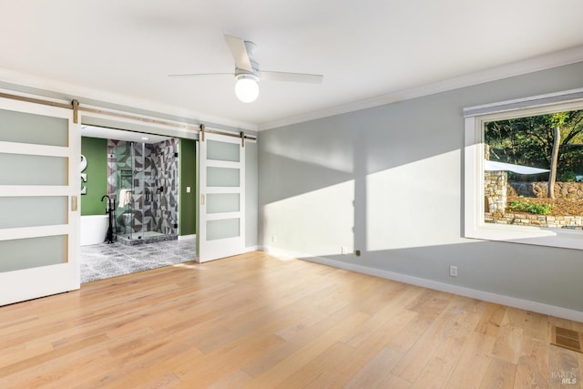 unfurnished room featuring ornamental molding, ceiling fan, a barn door, and wood finished floors