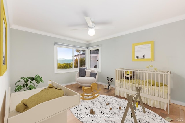 bedroom featuring crown molding, ceiling fan, wood finished floors, a crib, and baseboards