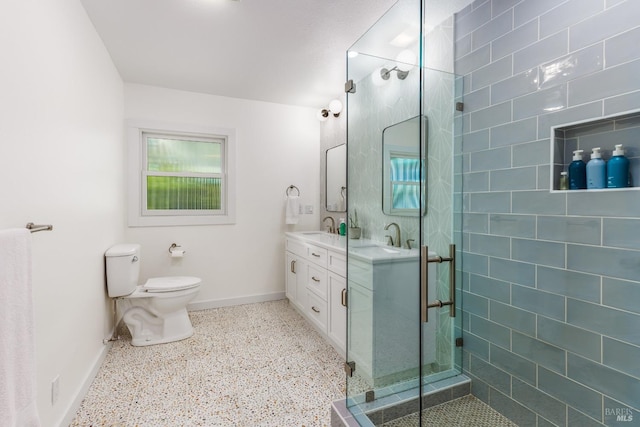 bathroom featuring toilet, speckled floor, a sink, a shower stall, and double vanity