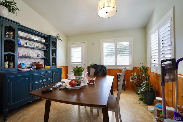 dining area with lofted ceiling, wainscoting, and wooden walls