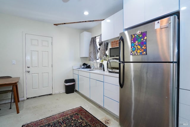 kitchen with light countertops, freestanding refrigerator, white cabinetry, a sink, and concrete flooring