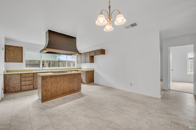 kitchen with visible vents, a kitchen island, wall chimney range hood, an inviting chandelier, and brown cabinetry