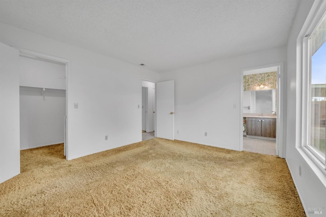 unfurnished bedroom with a textured ceiling, a walk in closet, connected bathroom, and light carpet