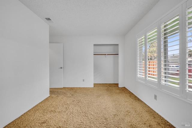 unfurnished bedroom featuring a closet, visible vents, a textured ceiling, and carpet